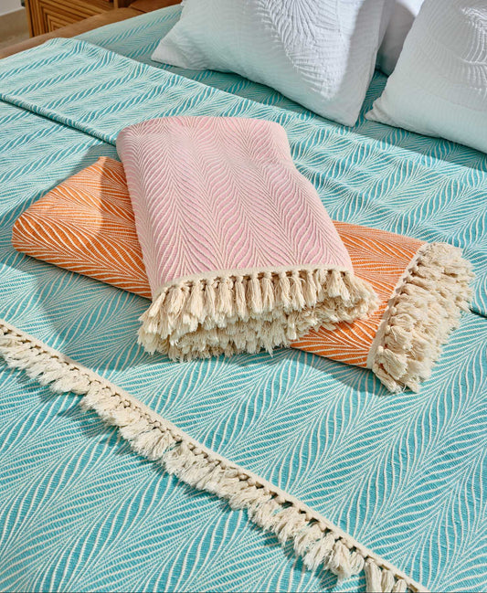 Pink, Orange & Blue blankets with tassels on a bed with the blue blanket setup as a cover
